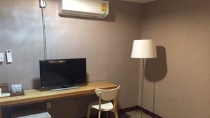 Una habitación pequeña y limpia con escritorio, silla, televisor, aire acondicionado, lámpara y refrigerador pequeño.