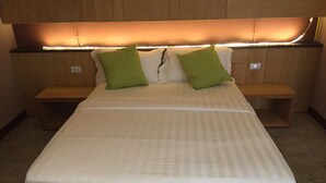 Una cama con un colchón blanco y dos almohadas verdes, con mesitas de noche de madera a cada lado.