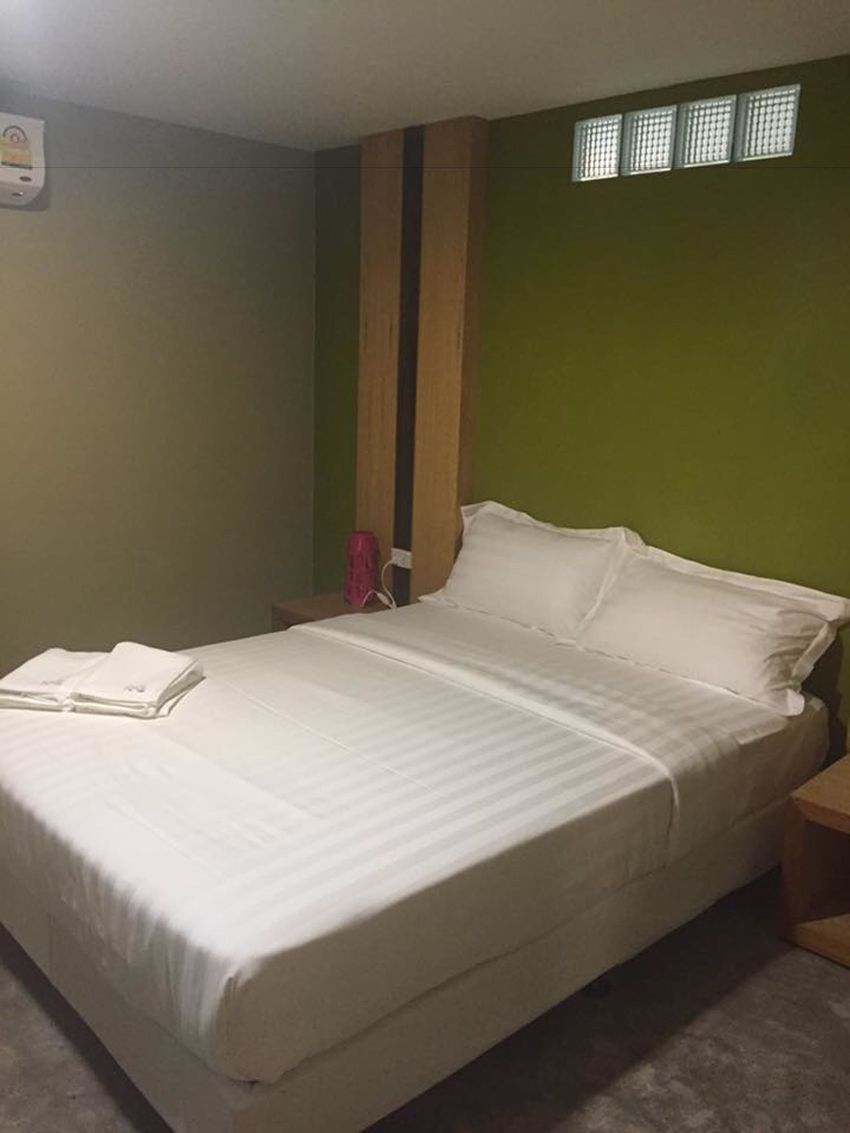 Cama bem arrumada com lençóis brancos em quarto com paredes verdes e cabeceira de madeira.