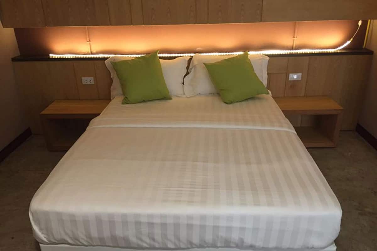 A bed with a white mattress and green pillows, wooden headboard, bedside tables, and a carpeted floor.