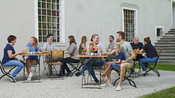A group of people seated at wooden tables outdoors, with a building in the background.