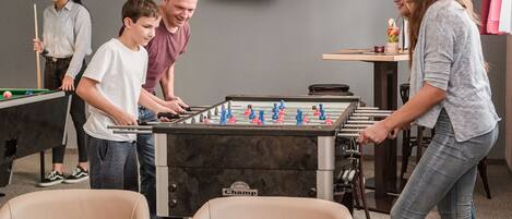 A foosball table in a room with a pool table and a television.