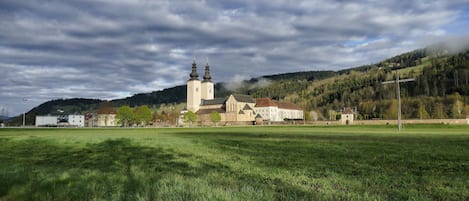 Una iglesia con un campanario, rodeada por un campo verde y una colina arbolada.