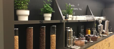 Un área de buffet con diferentes dispensadores de alimentos, platos y una máquina de café.