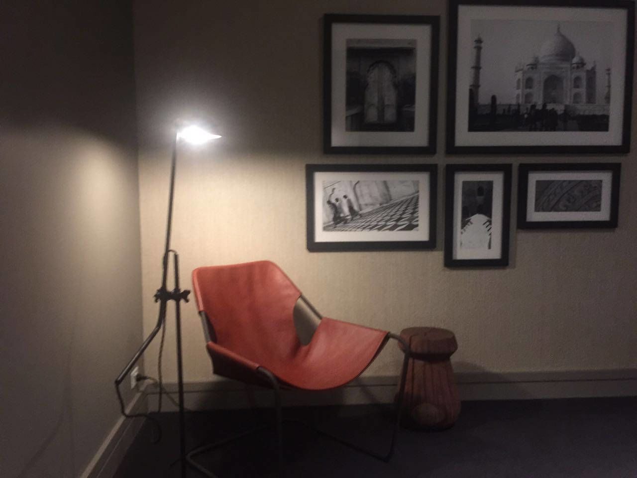 A room with a red chair, a floor lamp, and four framed pictures on the wall.