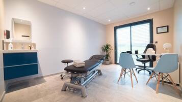 Experience a calm and professional atmosphere in this well-equipped examination room with a medical table, desk, and large window.