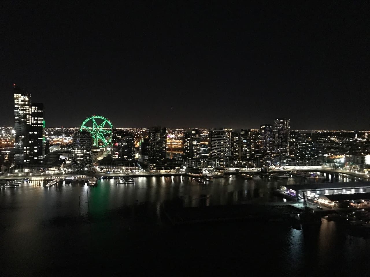 A nighttime cityscape with a prominent Ferris wheel and a bridge over a body of water.