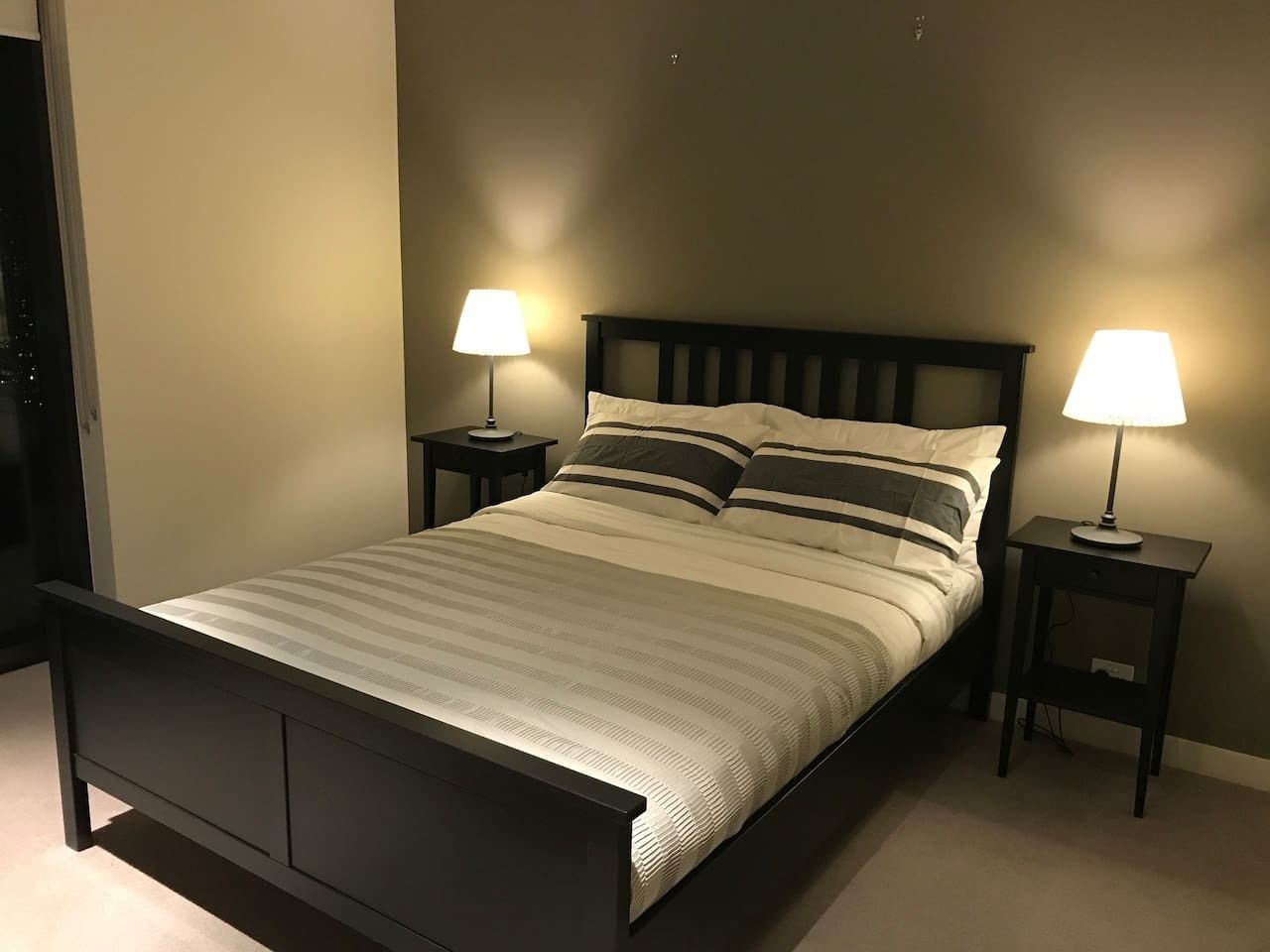 Una cama bien hecha con un edredón a rayas, dos mesitas de noche con lámparas y un cabecero de madera oscura.