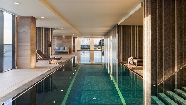A modern indoor swimming pool with a glass floor, a lounge area with seating, and a view of the cityscape. - Melbourne Docklands Convesso Seaview Apartment (Docklands)