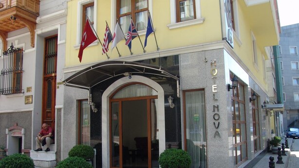 Ein Hotel Eingang mit überdachter Vorfahrt, einem Schild mit der Aufschrift "HOTEL NOVA" und Flaggen von der Türkei, den USA, dem Vereinigten Königreich und Deutschland.