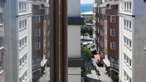 Blick aus einem Fenster auf eine Straße mit Gebäuden an beiden Seiten, einem klaren Himmel und weiter Wasserfläche.