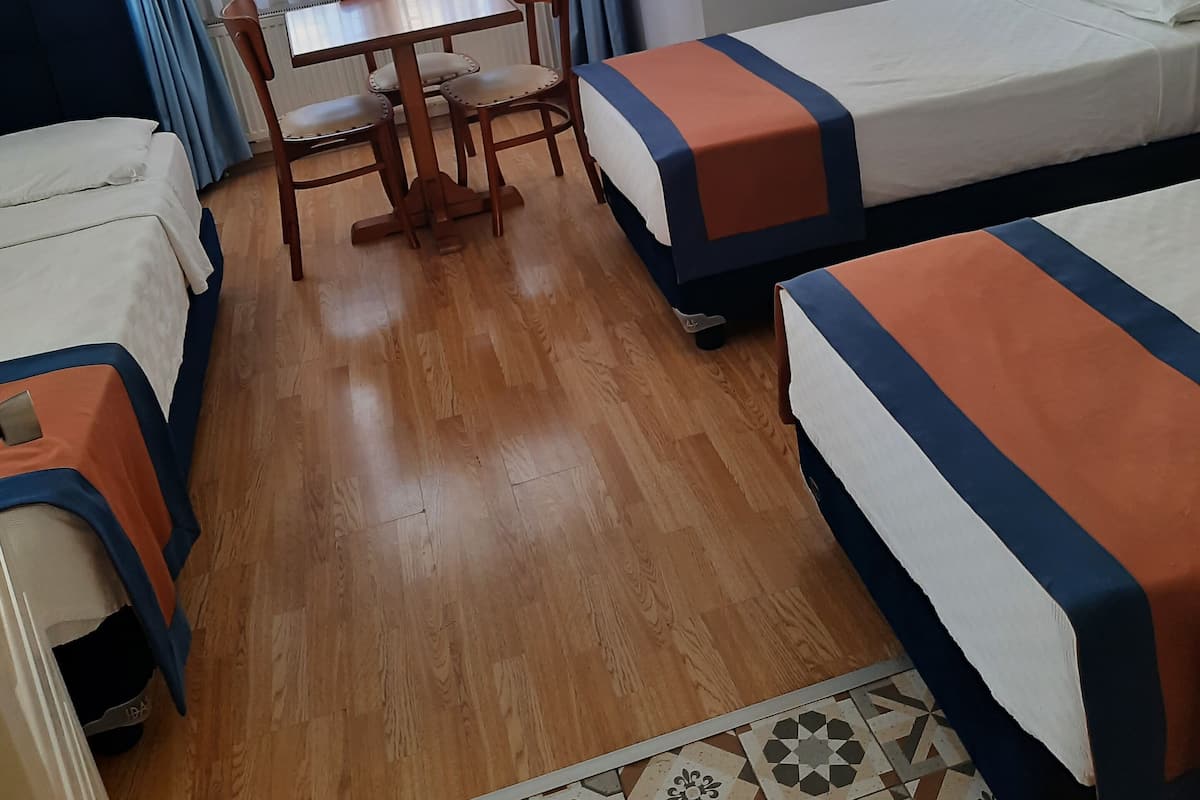 Une chambre d’hôtel avec deux lits simples, une table en bois avec des chaises et une fenêtre avec des rideaux bleus.