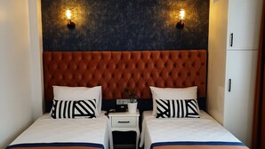 Ein Hotelzimmer mit zwei Betten, einem gepolsterten Kopfteil, zwei Wandleuchten, einem kleinen Nachttisch und einem weißen Kleiderschrank.