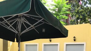 Eine Terrasse im Freien mit Tischen, Stühlen, einem grünen Sonnenschirm und Topfpflanzen.