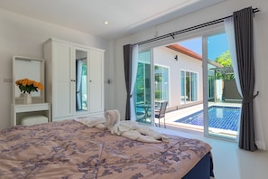 A bedroom with a bed, a desk, a chair, and a view of a swimming pool through a glass door.