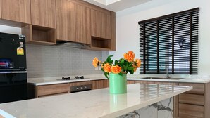 A modern kitchen with wooden cabinets, a marble island, and a vase of orange flowers. - Private Villa with Pool near Laguna (Choeng Thale)