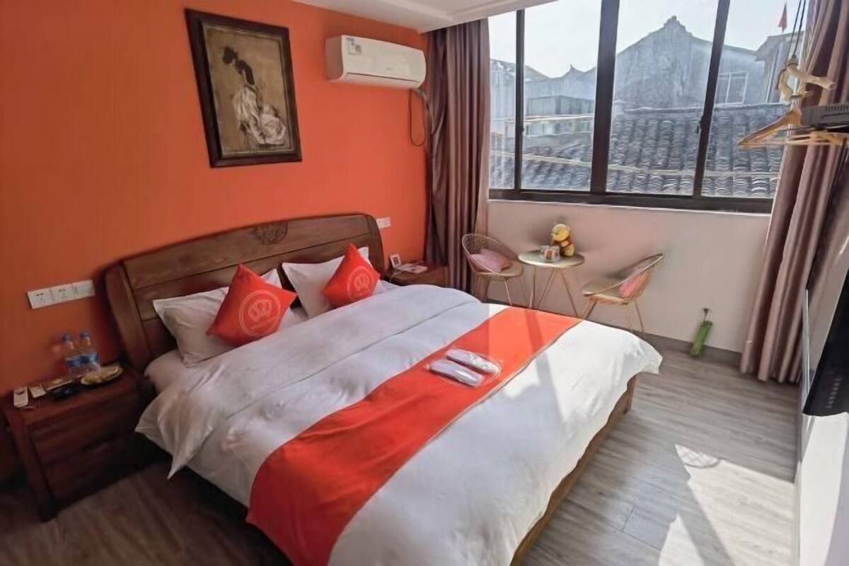 A hotel room with a bed, a small table, a chair, and a window with a view.