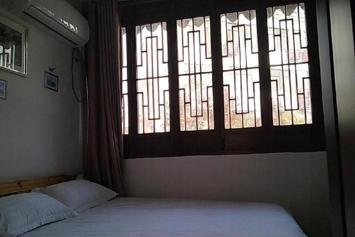 A bedroom with a bed, a window with decorative bars, an air conditioning unit, and a curtain.