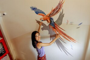 Una persona dipinge un grande murale raffigurante un uccello su un muro.