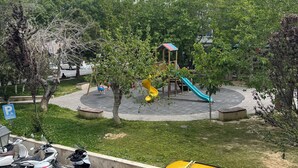 A yellow minivan parked in a lot with a playground in the background. - Karya Hotel (Kusadasi)