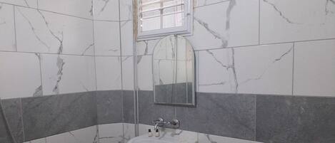 Un bagno con lavandino, specchio, WC, doccia e una finestra con persiane.