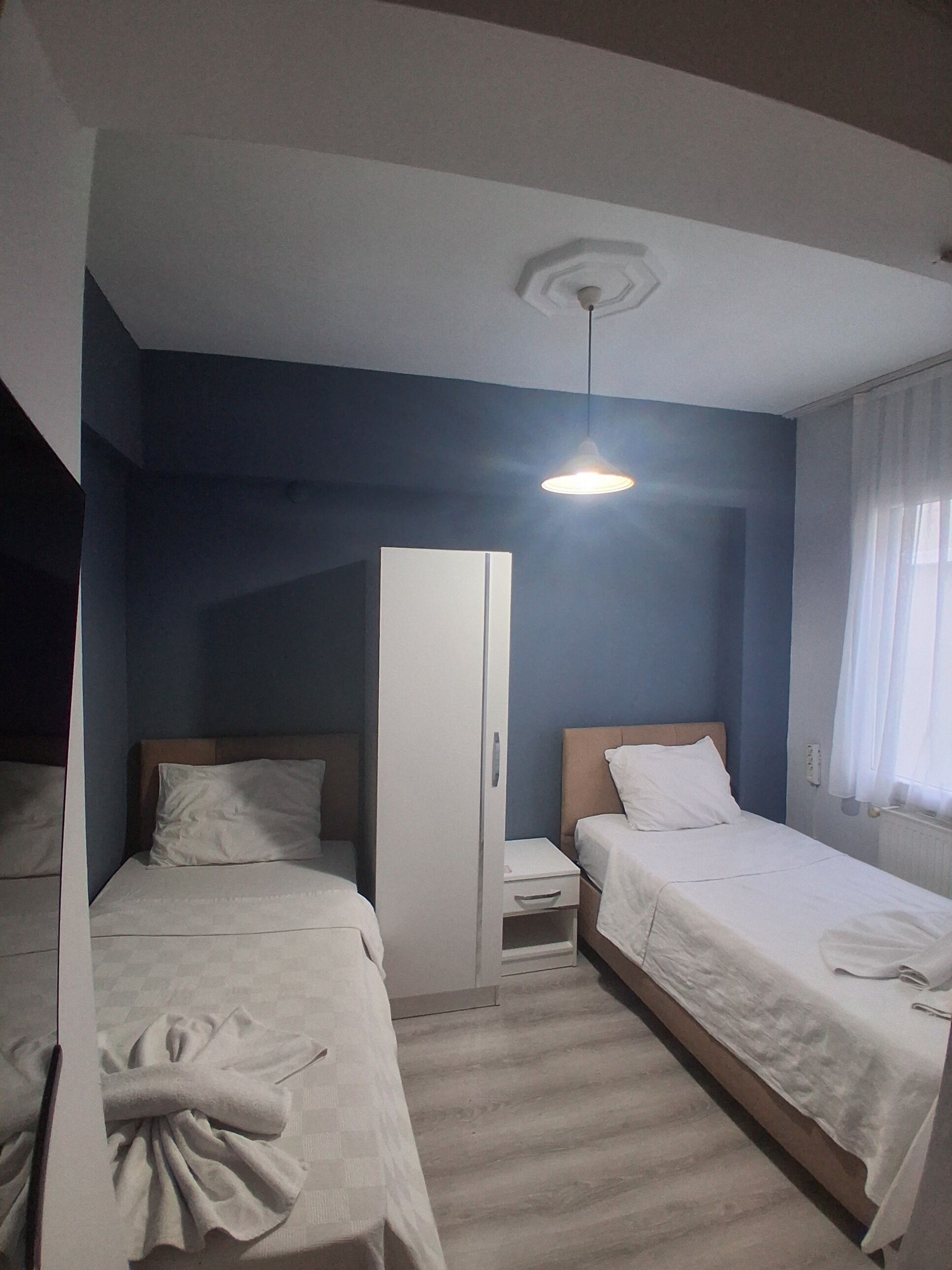 Un dormitorio con dos camas, un armario, una mesita de noche y una lámpara colgante.