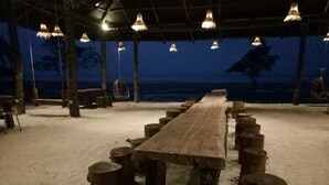 A long wooden table with stools in a covered outdoor area with hanging lights. - Koh Rong Love Resort - Hostel (Koh Rong)