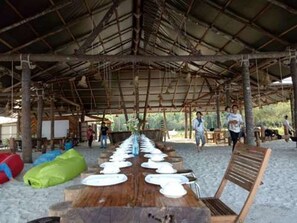 A covered outdoor dining area with a long wooden table set with plates and benches.