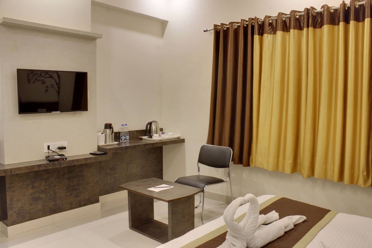 Une chambre d’hôtel équipée d’un téléviseur à écran plat fixé au mur, d’une petite table avec une chaise, d’un lit avec une serviette blanche et d’une fenêtre avec des rideaux jaunes.
