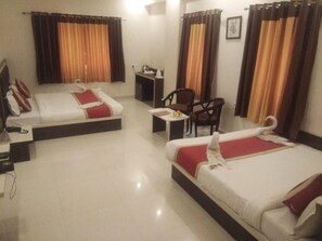 A hotel room with two beds, a desk, a chair, and a small table with a lamp. - The Byke Riddhi Inn (Udaipur)