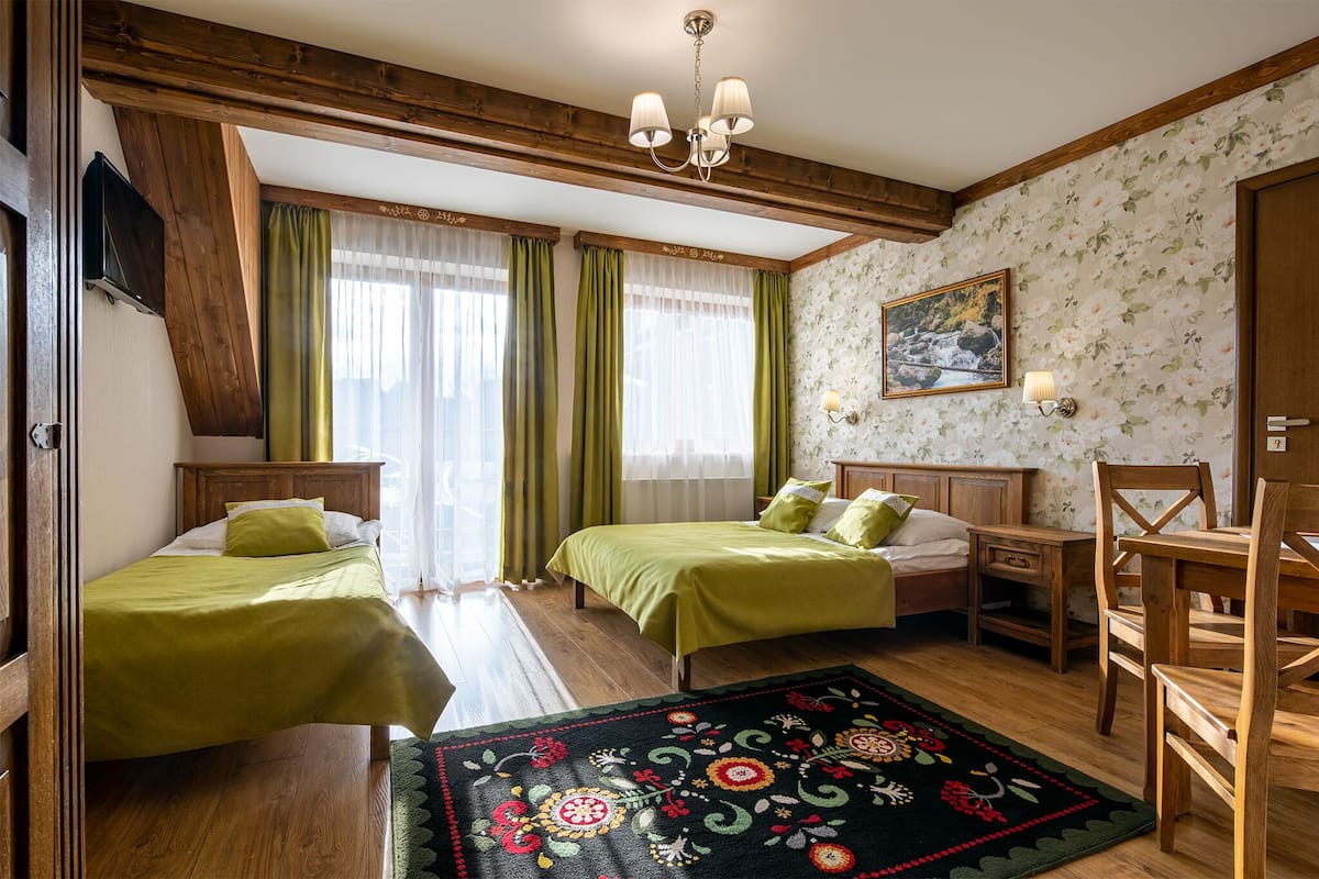 Una habitación con dos camas, techo de madera, candelabro, papel tapiz floral y una alfombra.