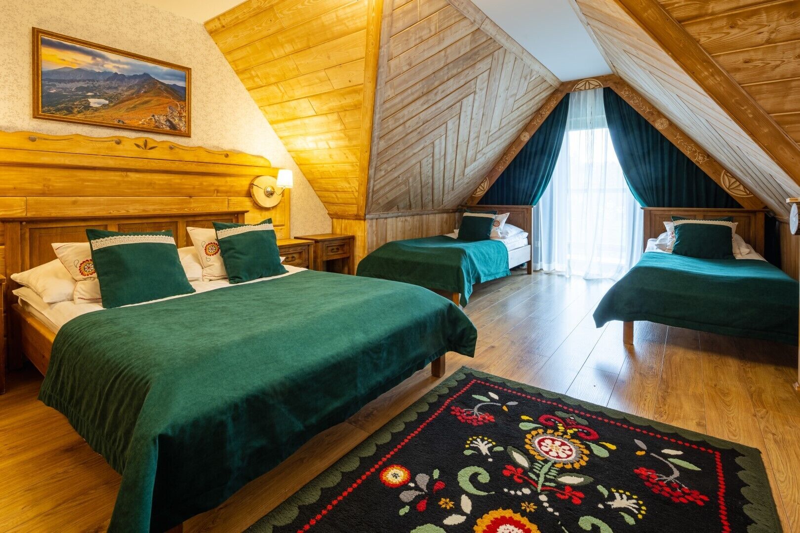 A cozy attic bedroom with two beds, wooden walls, a large window, and a decorative rug.