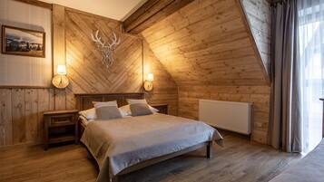 A cozy wooden bedroom with a bed, two bedside lamps, a picture on the wall, and a deer head decoration.