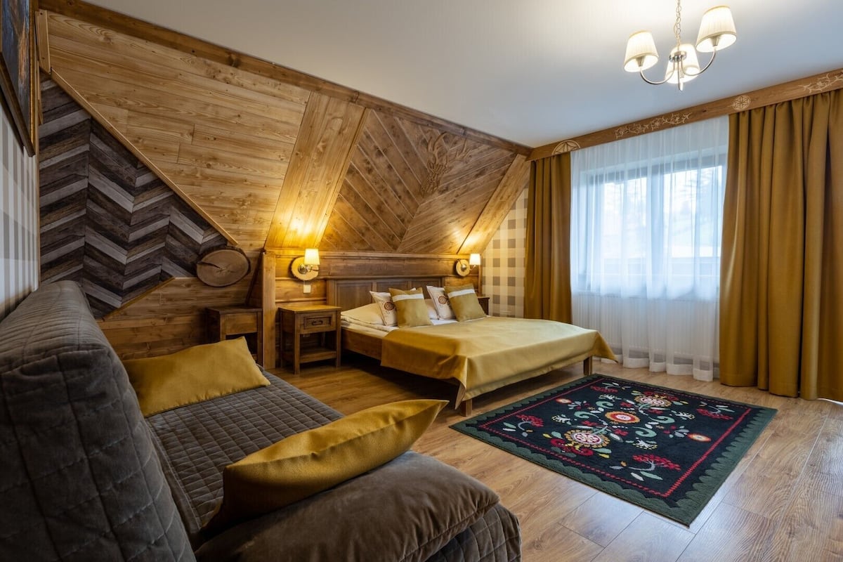 Un dormitorio acogedor con techo de madera, dos camas, un sofá y un tapete decorativo.