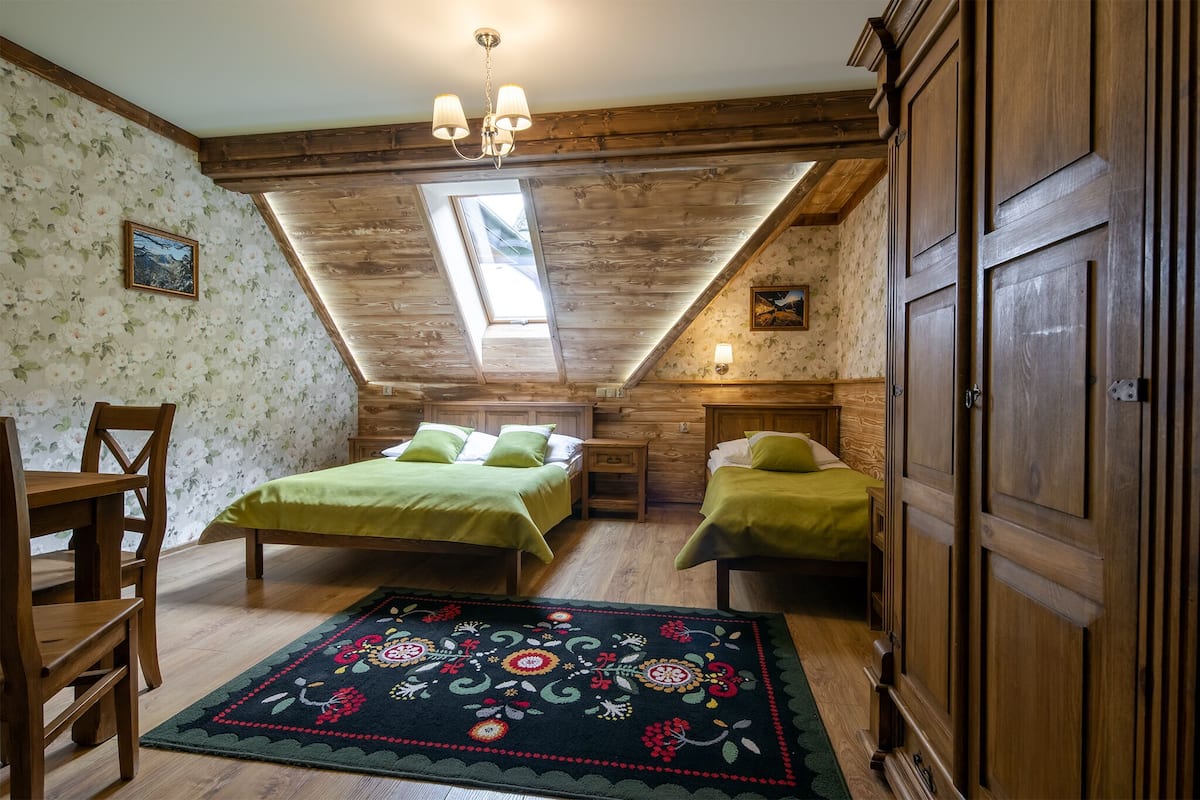 Un dormitorio con dos camas, techo de madera, tragaluz, candelabro y alfombra floral.