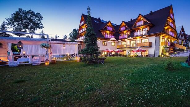 A large, multi-story building with a traditional architectural style, featuring balconies and a well-lit facade. - Kraina Smaku (Zakopane)