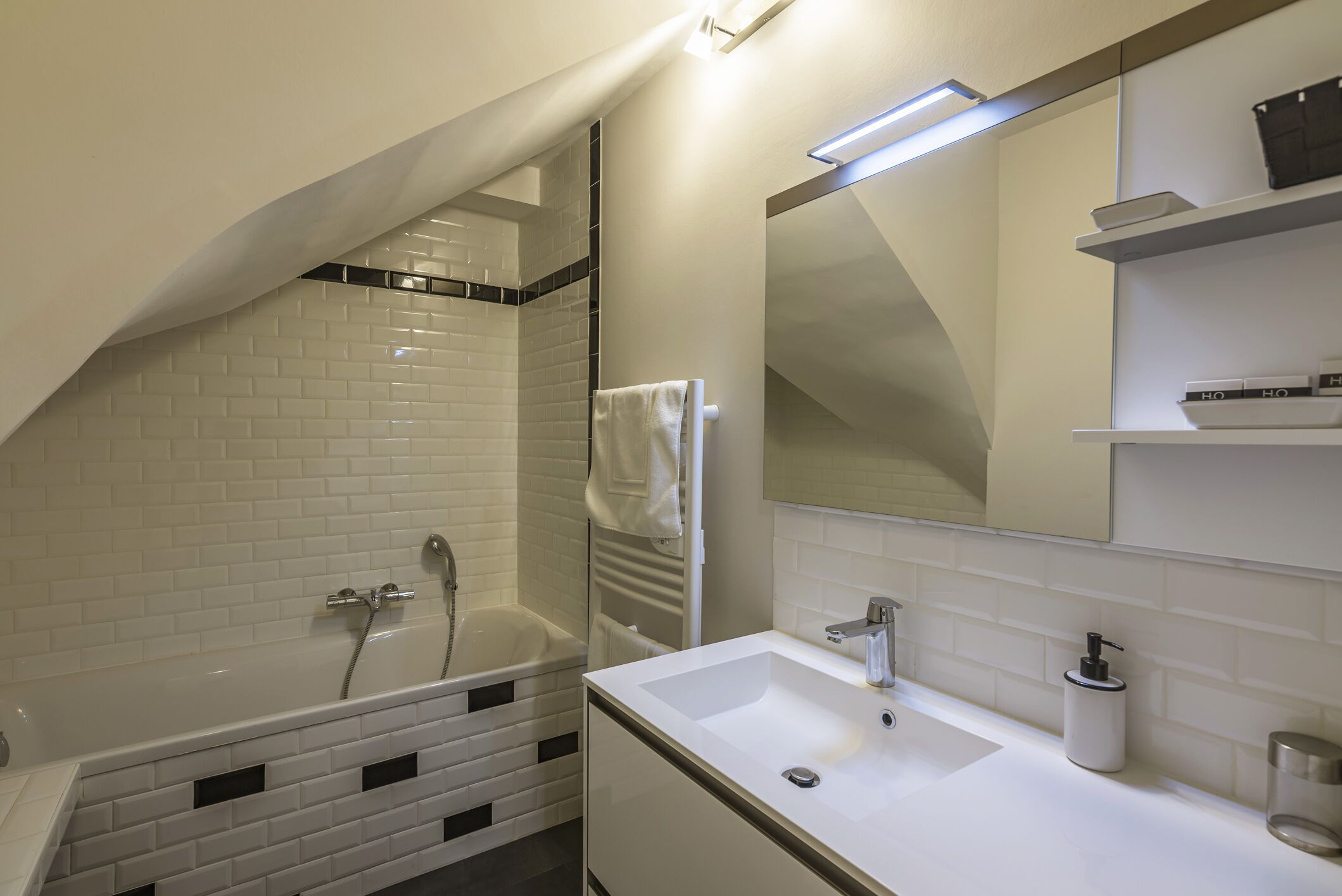 A modern bathroom with a white-tiled shower, a bathtub, a white sink with a mirror, and a shelf with toiletries.