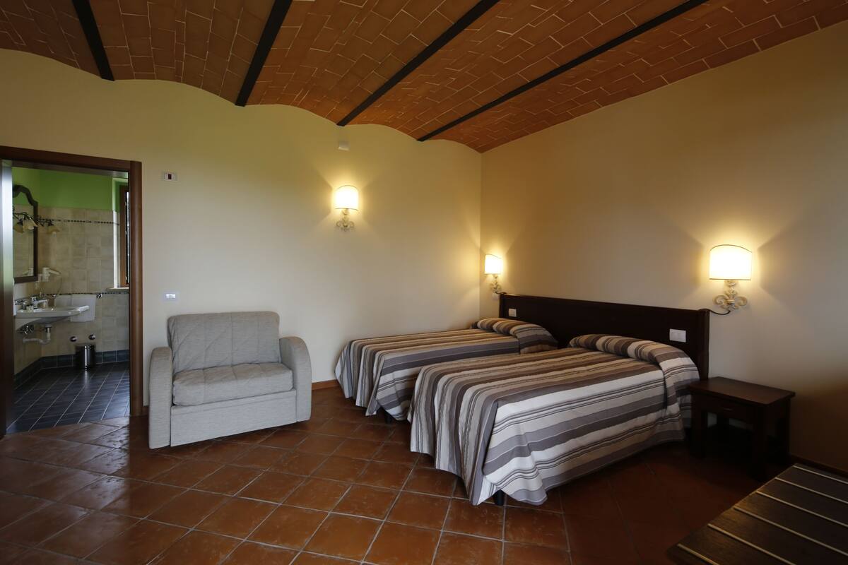 A room with two beds, a sofa, and a small table. There is a bathroom visible through an open door.