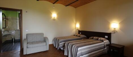 Habitación con dos camas, un sofá y una mesita. Se ve un baño a través de una puerta abierta.