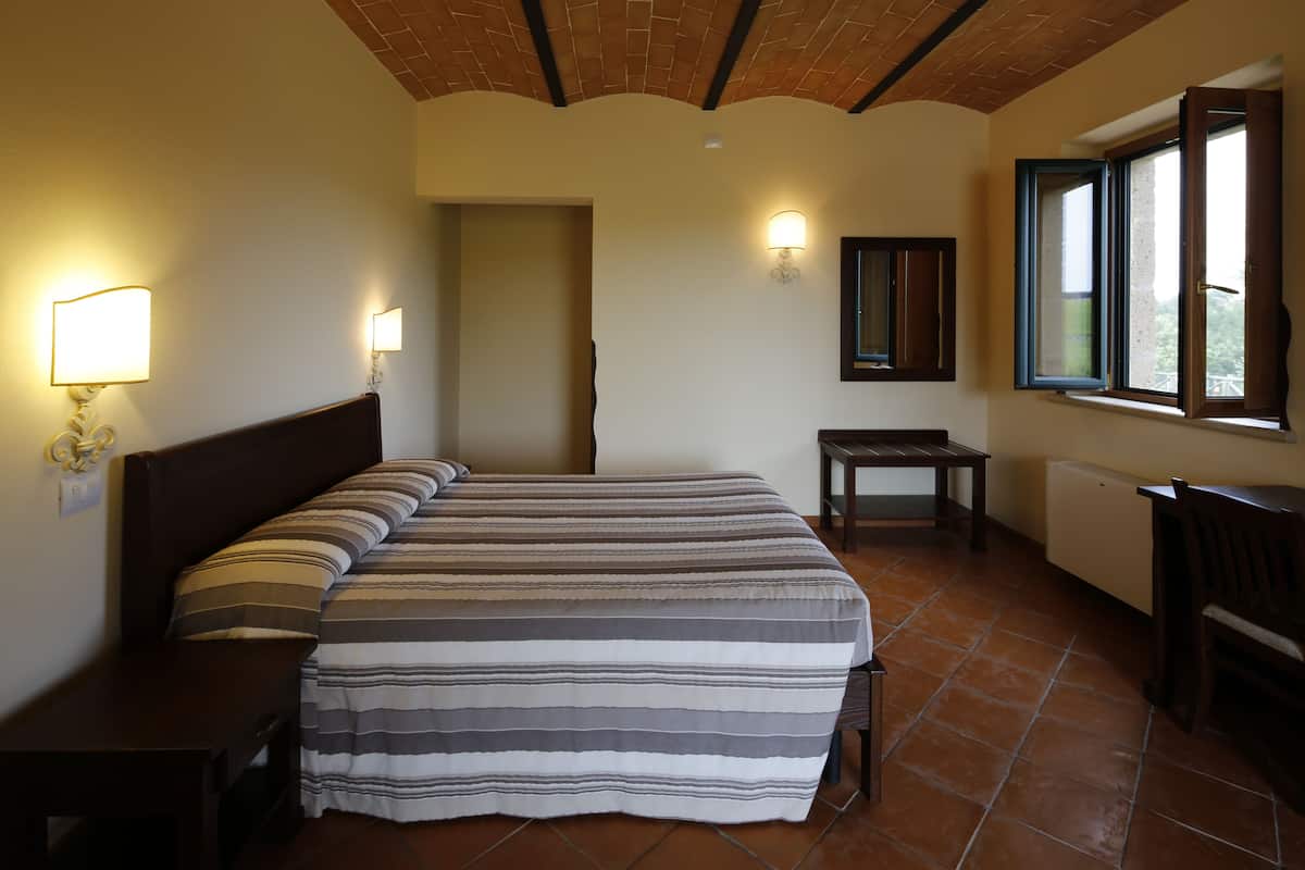 A bedroom with a large bed, two bedside tables, a nightstand, a desk, a chair, a window, and a door.