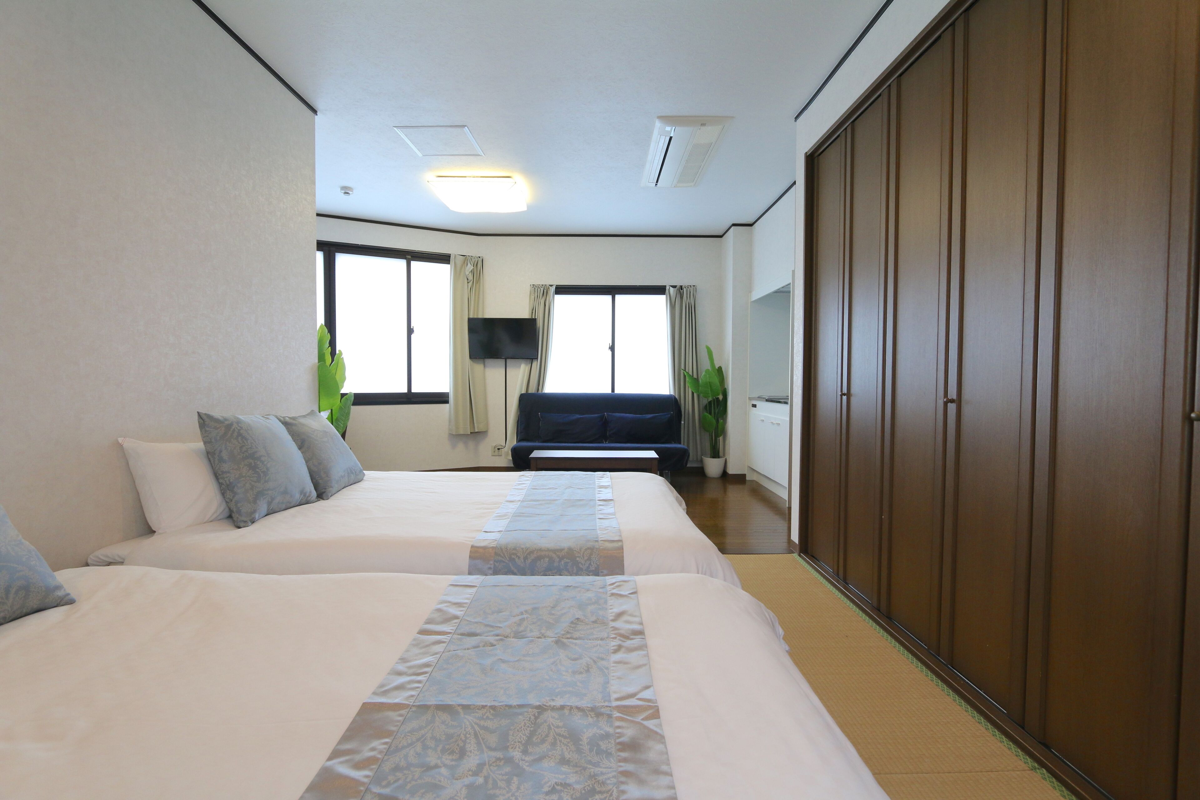 A hotel room with two beds, a TV, a sofa, a wardrobe, and large windows.