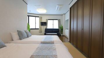 A hotel room with two beds, a TV, a sofa, a wardrobe, and large windows.