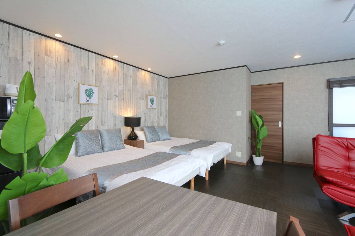 Ein modernes Hotelzimmer mit zwei Betten, einem Esstisch und einem roten Sessel.