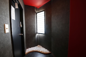 A narrow hallway with a dark door, a window with blinds, and a textured floor. - Guest House Liz Nakazaki-cho (Osaka)