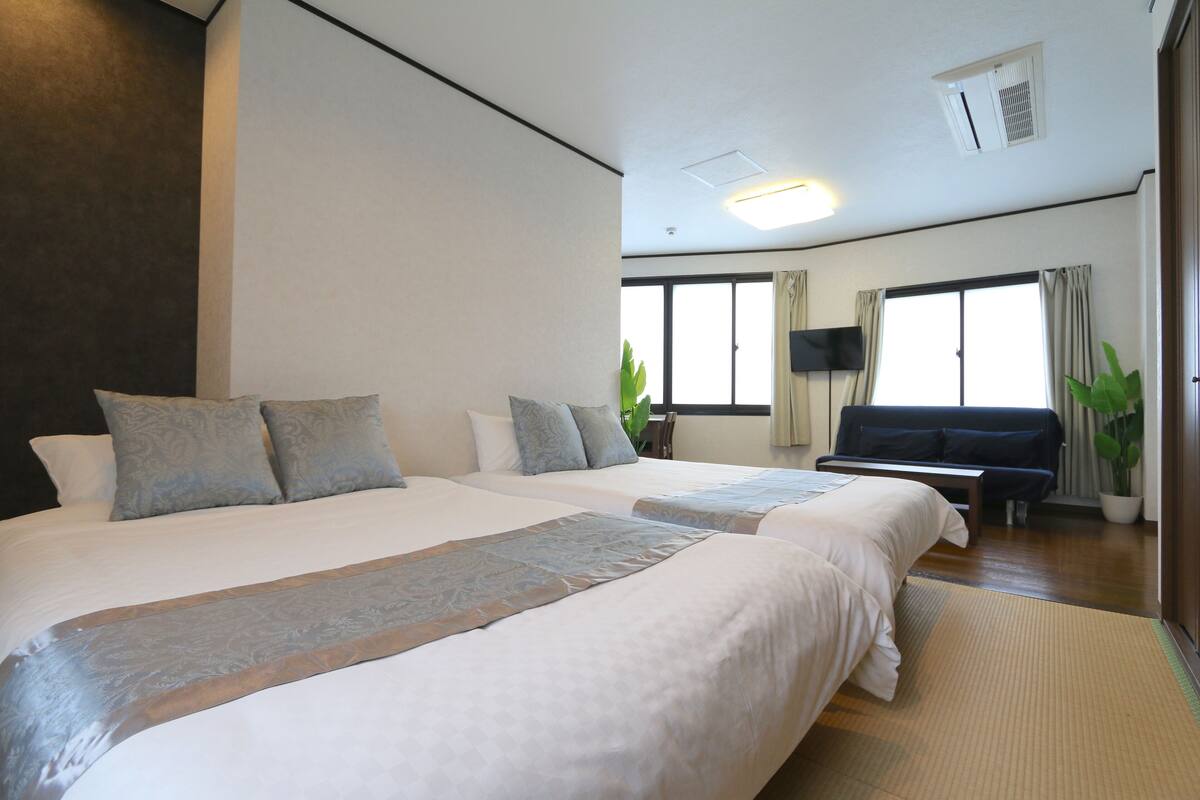 Ein Hotelzimmer mit zwei Betten, einem Flachbildfernseher, einem Sofa und großen Fenstern.