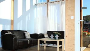 Una sala de estar moderna con un sofá de cuero negro, una mesa de centro de madera y cortinas blancas traslúcidas.