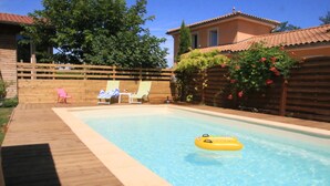 Una piscina con cubierta de madera, sillas de descanso y un flotador amarillo.