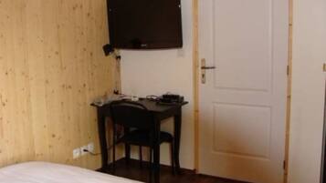 Ein kleines Zimmer mit einem Bett, einem Schreibtisch, einem Stuhl und einer Tür.