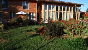 Una casa de madera de dos pisos con ventanas grandes y un jardín lleno de flores rojas.