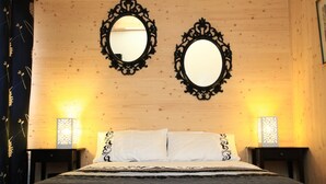 Un dormitorio con cabecera de madera, dos espejos ornamentados, ropa de cama blanca y dos mesitas de noche con lámparas.